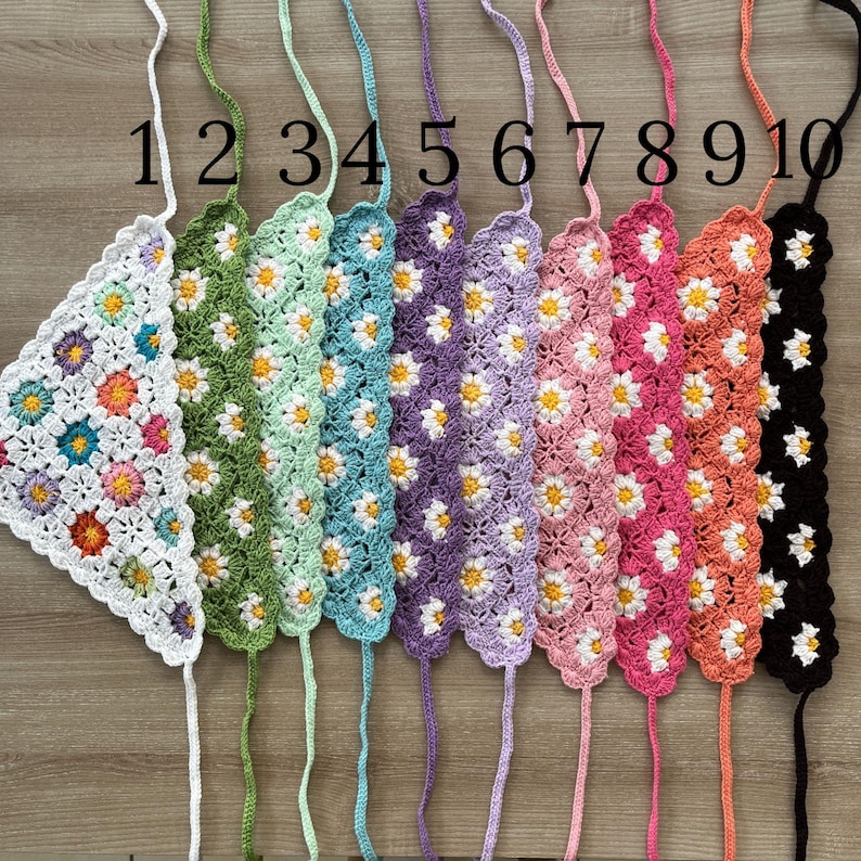 May include: A collection of ten crocheted triangle tops in various colors, each adorned with daisy patterns. The tops are numbered 1 through 10, with colors ranging from white to black, including green, purple, and pink.