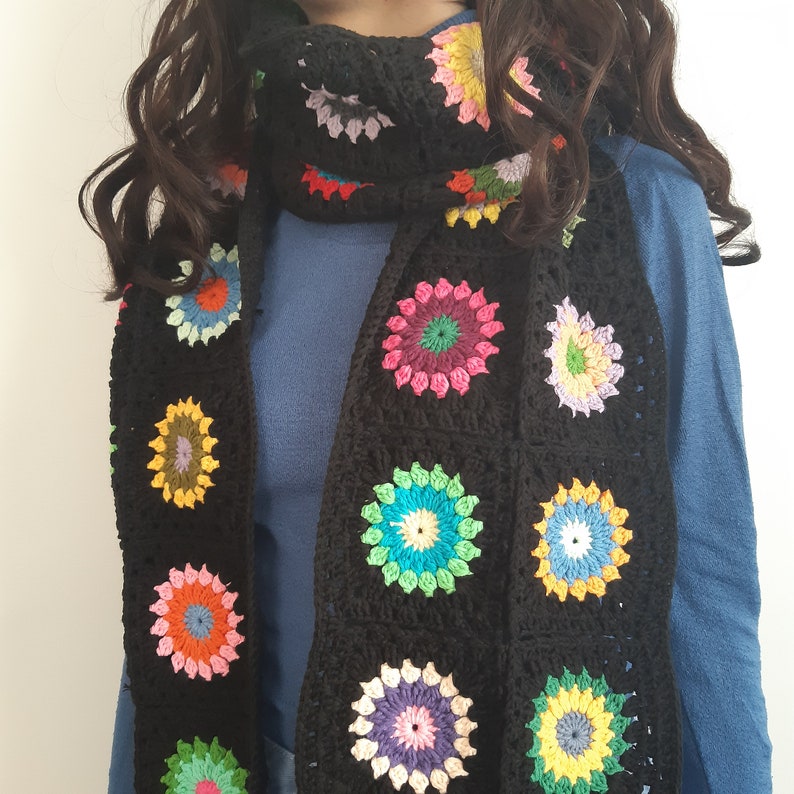 May include: A black crocheted scarf with colorful circular patterns. The scarf is made of yarn and has a variety of colors, including red, blue, green, yellow, and pink.