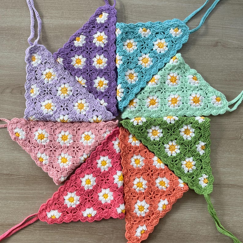 May include: Seven crocheted triangle shaped pieces with a daisy pattern in various colors, including purple, blue, green, pink, and orange.