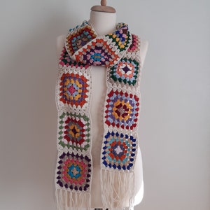 May include: A colorful crocheted scarf with a fringe. The scarf is made of squares with different colors, including red, orange, yellow, green, blue, and purple.
