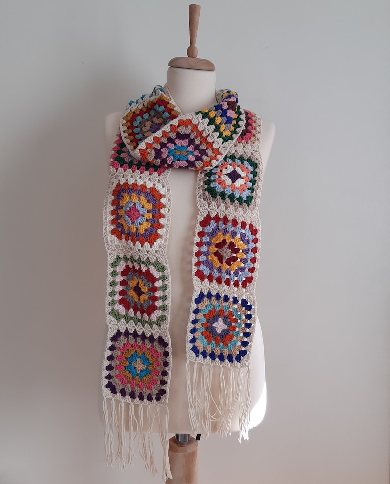 May include: A colorful crocheted scarf with a fringe. The scarf is made of squares with different colors, including red, orange, yellow, green, blue, and purple.