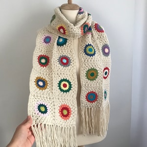 May include: A crocheted scarf with a white background and colorful circular designs. The scarf has fringe on the ends.