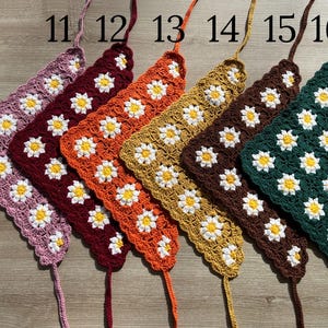 May include: Six crocheted triangle scarves in different colors, including pink, red, orange, yellow, brown, and green. Each scarf has a daisy pattern and is labeled with a number from 11 to 16.