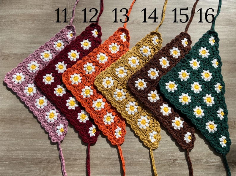 May include: Six crocheted triangle scarves in different colors, including pink, red, orange, yellow, brown, and green. Each scarf has a daisy pattern and is labeled with a number from 11 to 16.