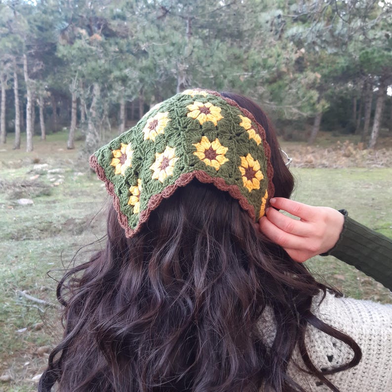 May include: A green and yellow crocheted sunflower headband with brown trim. The headband is tied at the back of the head.