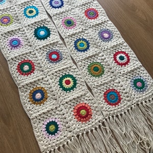 May include: Two crocheted table runners with fringe. Each runner is made of a beige yarn and features a repeating pattern of colorful circles.