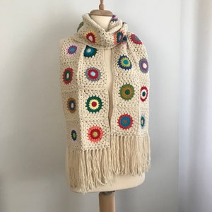 May include: A crocheted scarf with a fringe. The scarf is made of cream-colored yarn and features colorful circular motifs.