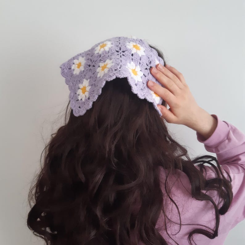 May include: A purple crocheted headband with white daisy flowers. The headband is worn on a person with long, dark brown hair.