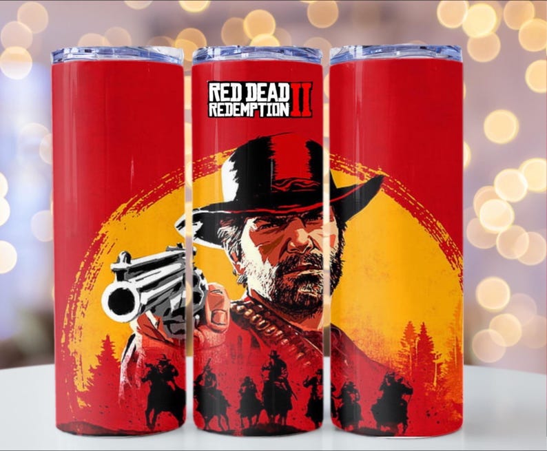 Puede incluir: Vaso rojo con un dise&ntilde;o gr&aacute;fico del videojuego Red Dead Redemption II. El dise&ntilde;o incluye un hombre con sombrero sosteniendo un arma, sobre un fondo de puesta de sol. El vaso es rojo con tapa plateada.