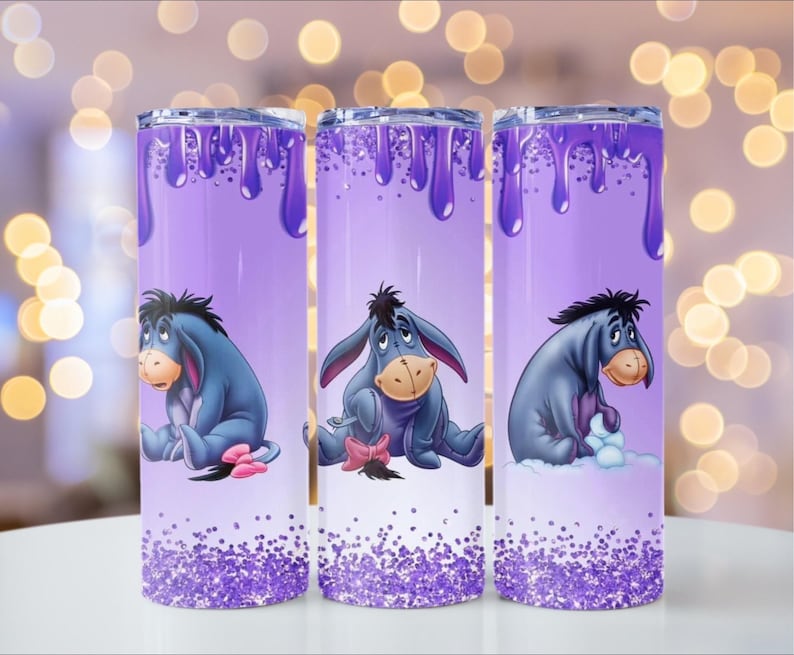 Puede incluir: Tres vasos t&eacute;rmicos morados con Eeyore de Winnie the Pooh. Cada vaso tiene un dise&ntilde;o de pintura goteando morada, un dibujo animado de Eeyore y una base brillante. El fondo est&aacute; borroso con luces bokeh.