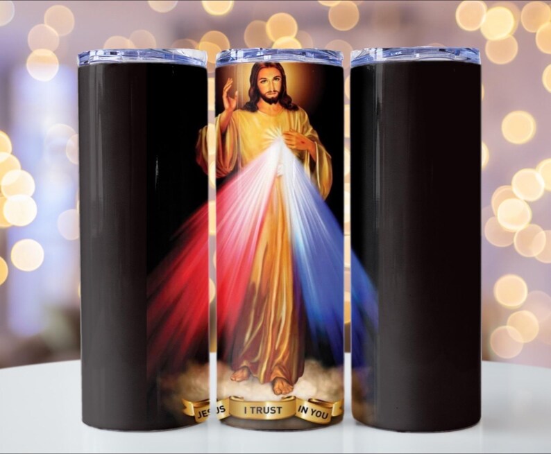 Puede incluir: Un vaso de acero inoxidable con un dise&ntilde;o envolvente que presenta una imagen religiosa de Jesucristo. La imagen tiene una combinaci&oacute;n de colores dorados, rojos y azules. El vaso tiene un fondo negro y una tapa transparente.