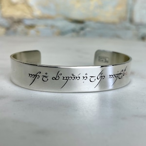 May include: Silver bracelet with an inscription in Elvish script that reads "One Ring to rule them all, One Ring to find them, One Ring to bring them all and in the darkness bind them."