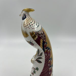 May include: A white porcelain figurine of a pheasant with gold, red, green, and blue accents. The pheasant is standing on a base with floral designs.