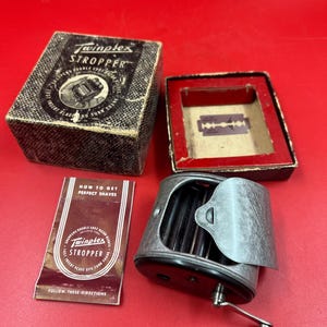 May include: A vintage Twinplex Stropper razor blade sharpener with a metal crank, accompanied by its original cardboard box featuring the text Twinplex Stropper, a separate box lid with a red interior, and a small instructional booklet titled How to Get Perfect Shaves.