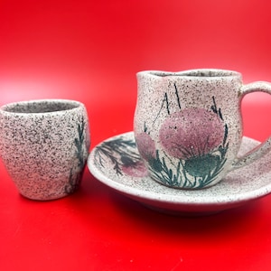 May include: A white ceramic teacup and saucer set with a floral design. The cup has a handle and the saucer has a scalloped edge.