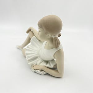 Puede incluir: Una figurita de porcelana de una ni&ntilde;a joven con un tut&uacute; blanco y sentada con las piernas cruzadas. Su cabello est&aacute; recogido en una coleta.