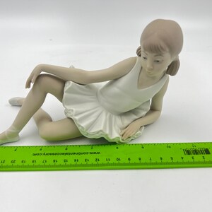 Puede incluir: Una figurita de porcelana de una ni&ntilde;a peque&ntilde;a con un tut&uacute; blanco y sentada con las piernas cruzadas. Tiene el pelo largo y casta&ntilde;o y mira hacia abajo.