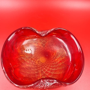 May include: A red glass bowl with a wavy rim and gold flecks throughout. The bowl is ideal for holding jewellery, trinkets, or other small items.