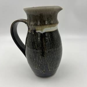 May include: A dark brown ceramic jug with a white and brown glaze. The jug has a wide mouth and a handle.