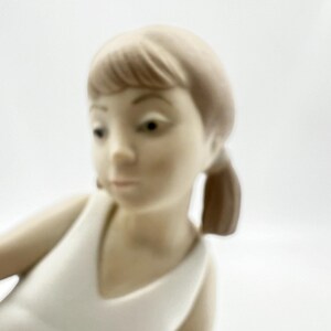 Puede incluir: Una figurita de porcelana de una ni&ntilde;a con cabello casta&ntilde;o que lleva un vestido blanco. La figurita est&aacute; en posici&oacute;n sentada con la cabeza inclinada hacia abajo.
