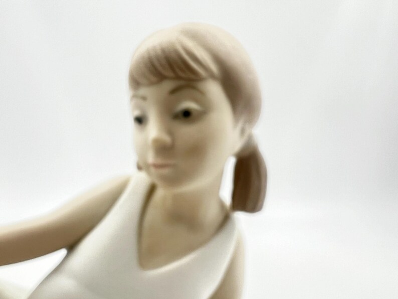 Puede incluir: Una figurita de porcelana de una ni&ntilde;a con cabello casta&ntilde;o que lleva un vestido blanco. La figurita est&aacute; en posici&oacute;n sentada con la cabeza inclinada hacia abajo.