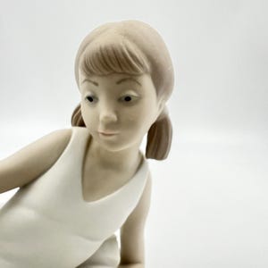 Puede incluir: Una figurita de porcelana de una ni&ntilde;a peque&ntilde;a con un vestido blanco. Tiene el pelo casta&ntilde;o y est&aacute; en posici&oacute;n de ballet.