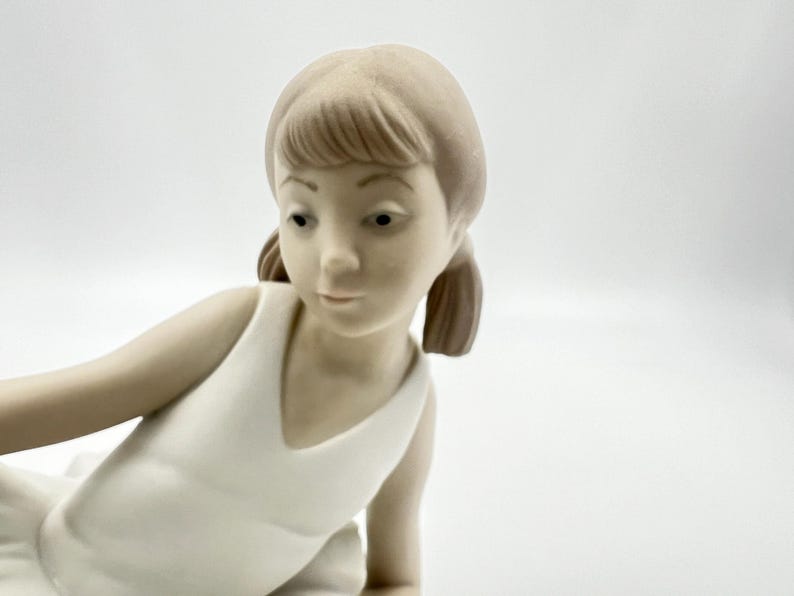 Puede incluir: Una figurita de porcelana de una ni&ntilde;a peque&ntilde;a con un vestido blanco. Tiene el pelo casta&ntilde;o y est&aacute; en posici&oacute;n de ballet.