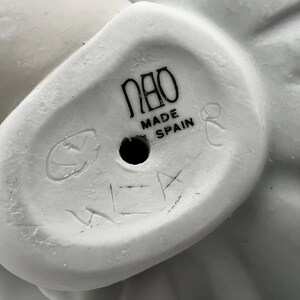 Puede incluir: Figurita de porcelana blanca con un dise&ntilde;o detallado. La base de la figurita tiene el texto "Nao Made in Spain" y un peque&ntilde;o agujero.