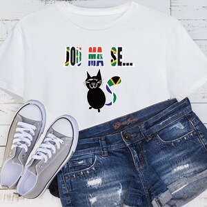 Pu&ograve; includere: Maglietta bianca con un gatto nero che indossa una coda di bandiera sudafricana e la scritta "Jou Ma Se..." stampata sul davanti. La maglietta &egrave; abbinata a pantaloncini di jeans blu e scarpe da ginnastica di tela grigie.