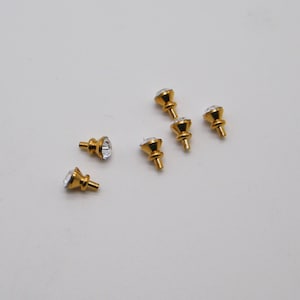 May include: Six gold-toned drawer pulls with clear crystal knobs. The pulls have a round base and a slightly raised, pointed top.