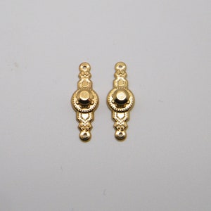 May include: Two gold-toned metal decorative pieces with ornate designs. Each piece features a round center with a raised knob and intricate floral patterns.