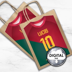 May include: Two brown paper gift bags with handles. The bags are decorated with a red and green soccer jersey design. The jersey has the name "Lucas" and the number "10" printed on it. The bags have a digital file label.