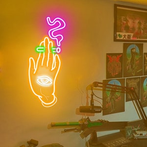 May include: A neon sign with a hand holding a cigarette and a question mark above it. The hand has an eye in the palm. The sign is on a yellow wall.