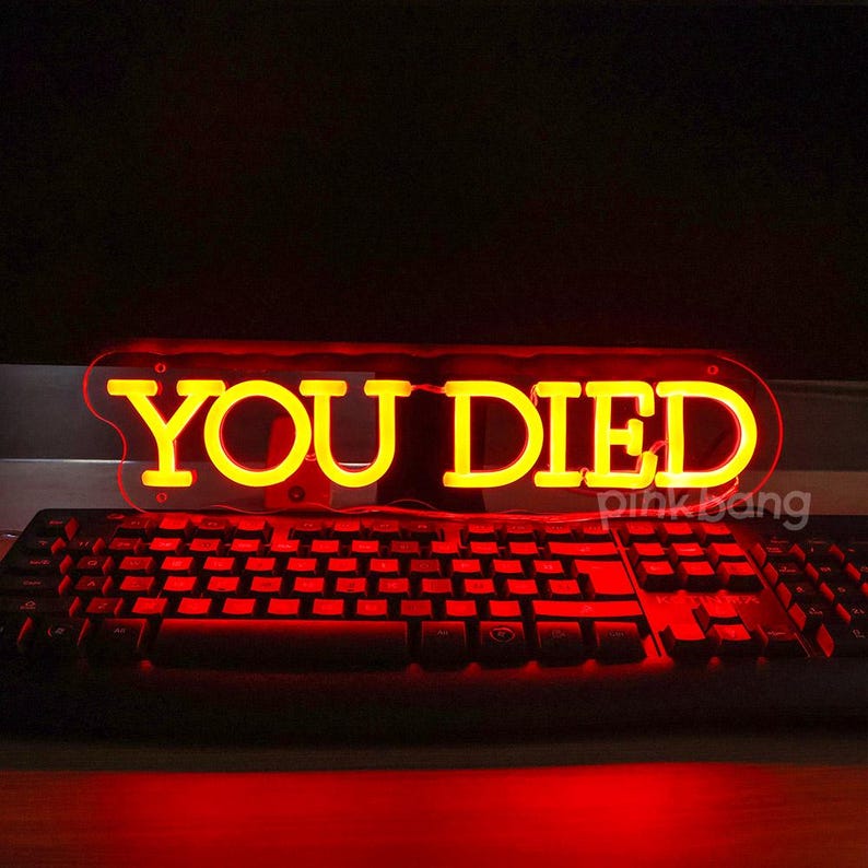 May include: A red neon sign with the words "YOU DIED" in yellow letters. The sign is sitting on top of a black keyboard.