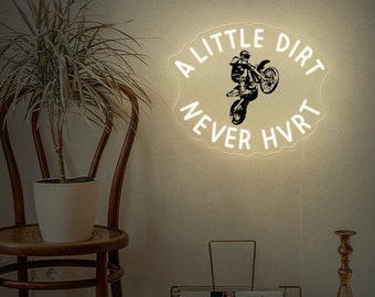 May include: A white neon sign with a black silhouette of a motocross rider jumping over a ramp. The sign reads "A little dirt never hurt".