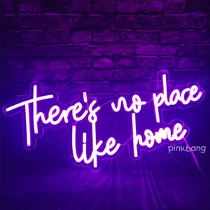 May include: Purple neon sign with white lettering that reads "There's no place like home". The sign is on a brick wall background.