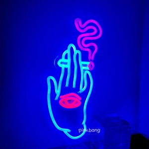 May include: Neon sign depicting a hand holding a cigarette with smoke rising above it. The hand is blue, the cigarette is white, and the smoke is pink. The sign has the text "pink bang" at the bottom.
