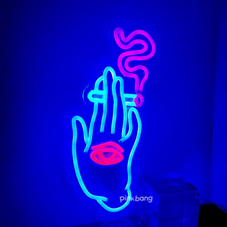 May include: Neon sign depicting a hand holding a cigarette with smoke rising above it. The hand is blue, the cigarette is white, and the smoke is pink. The sign has the text "pink bang" at the bottom.