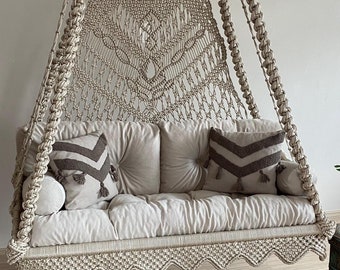 Könnte beinhalten: Eine beige Makramee-Hängematte mit einem weißen Kissen und zwei Kissen mit braunen Chevron-Mustern. Die Hängematte hängt von der Decke und auf dem Boden liegt ein beigefarbener gehäkelter Teppich.