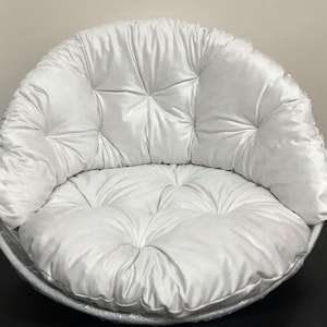 May include: A white, round, tufted cushion with a large, round, tufted seat. The cushion is made of a soft, plush fabric.