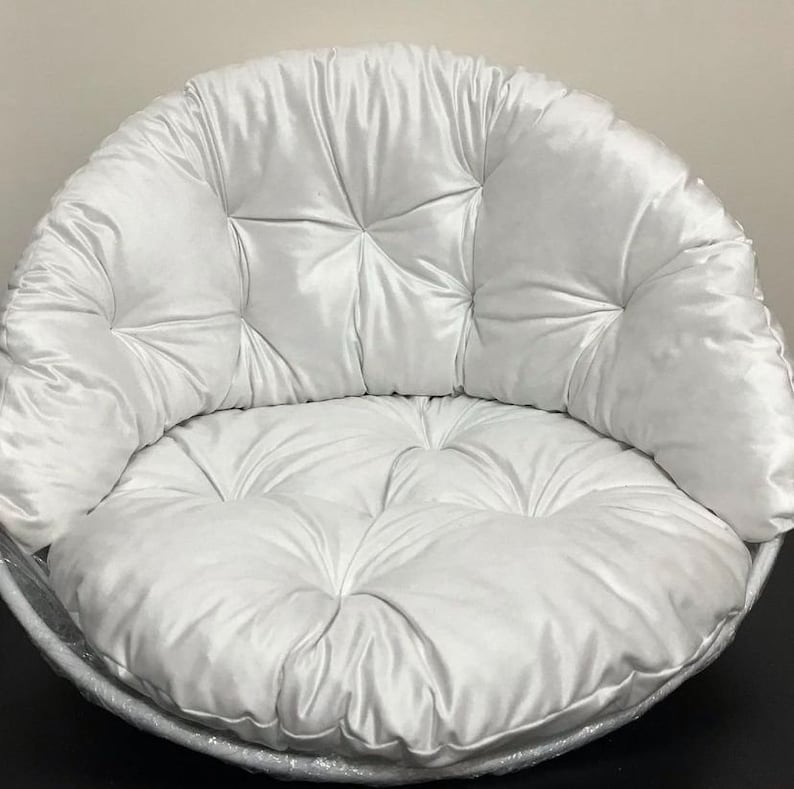 May include: A white, round, tufted cushion with a large, round, tufted seat. The cushion is made of a soft, plush fabric.