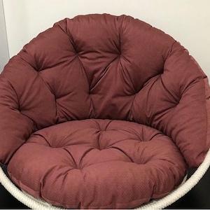 May include: A large, round, brown, cushioned chair with a white rope frame. The chair has a deep, comfortable seat and a high back.