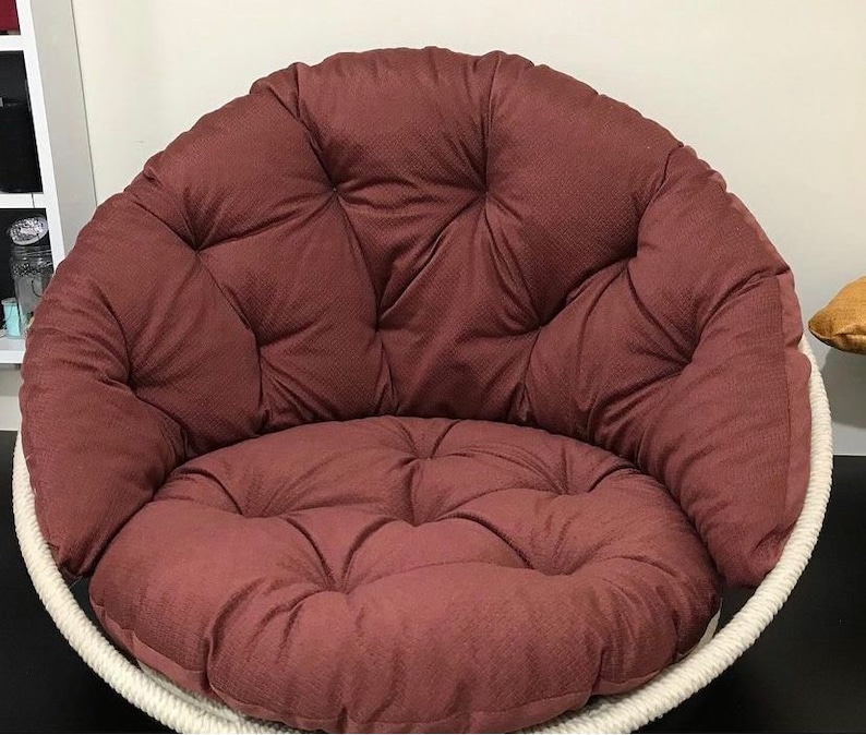 May include: A large, round, brown, cushioned chair with a white rope frame. The chair has a deep, comfortable seat and a high back.