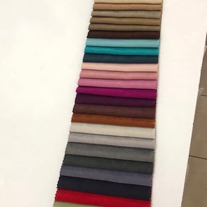 May include: A collection of fabric swatches in various colors, including beige, brown, teal, pink, purple, maroon, orange, gray, dark gray, navy blue, red, and green. The swatches are arranged vertically in a row.
