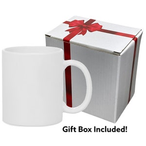 May include: A white ceramic mug with a handle. The mug is in a white gift box with a red ribbon and bow.