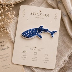 May include: A whale shark embroidered patch in shades of blue and white with a spotted pattern, mounted on a cream-coloured card. The card features the text STICK ON, EASY TO APPLY, and instructions: 1. HEAT, 2. PRESS firmly for 30 seconds, 3. ENJOY.