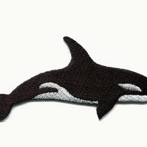 Puede incluir: Un parche bordado termoadhesivo con forma de orca. El diseño presenta un cuerpo negro con detalles en blanco en la mancha ocular, la parte inferior de la mandíbula y una marca blanca curva a lo largo del costado del torso cerca de la aleta dorsal.
