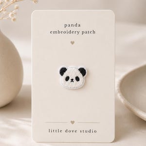 May include: A small panda embroidery patch featuring a white face with black ears and eye patches, centred on a rectangular cream-coloured display card. The card displays the text panda embroidery patch and little dove studio with heart icons.