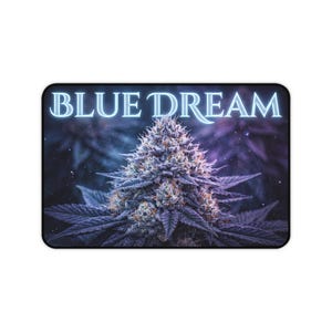 May include: A rectangular desk mat featuring a central image of a cannabis flower with purple and blue hues. The text BLUE DREAM is printed in a glowing light blue font across the top portion of the mat against a dark, hazy background.