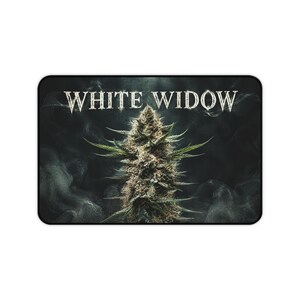 May include: A rectangular desk mat featuring a central cannabis flower bud surrounded by swirling gray smoke against a dark background. The text WHITE WIDOW is printed in a bold, white, serif font across the top center of the mat.